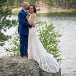Groom kissing the bride on the temple at Legion Lake on top of the rocks with the lake in the background and green pine trees flanking the left side of the image.