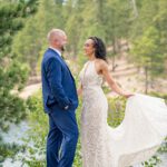 Bride and groom wedding portrait on top of the rocks at Legion Lake in Custer State Park in the summer with the green pine trees and the grooms navy blue suit.