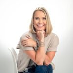 Branding image of a blonde woman sitting in a white chair with her hand supporting her chin on a white backdrop in the studio.