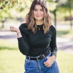 Senior Girl with a great smile outside with green trees surrounding her outdoors summer day black shirt blue jeans smiling senior photos pictures